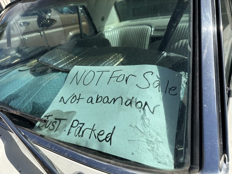 A handwritten sign on a car windshield reads, "NOT For Sale. Not abandon. Just Parked," seen from outside the vehicle.