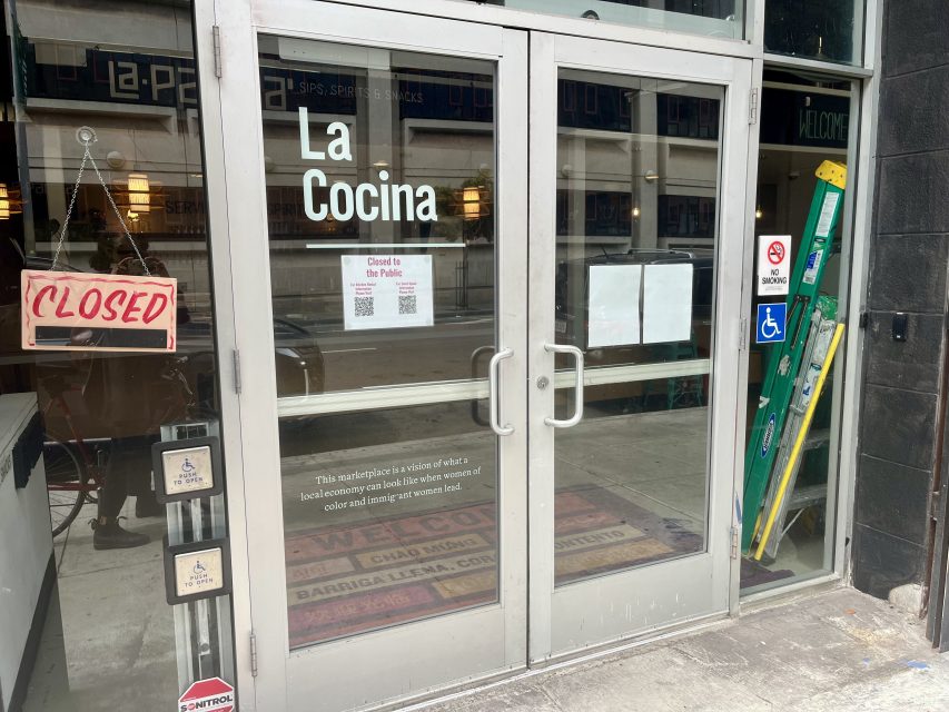 Glass doors of a restaurant named "La Cocina" with a "Closed" sign, various notices, and a step ladder leaning against the wall outside.