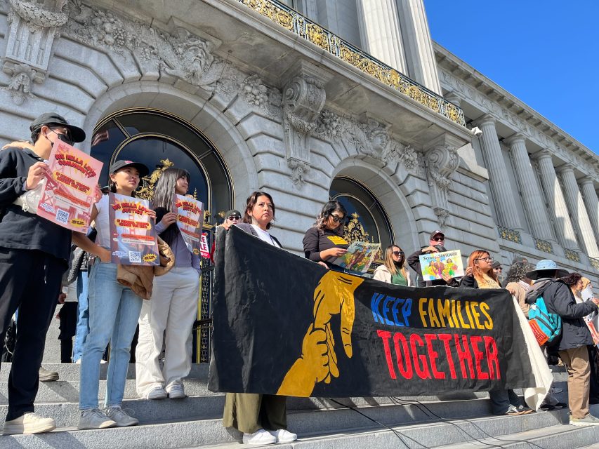 A group of people stand on government building steps holding signs and a large banner that reads "Keep Families Together" during an immigration protest or demonstration.