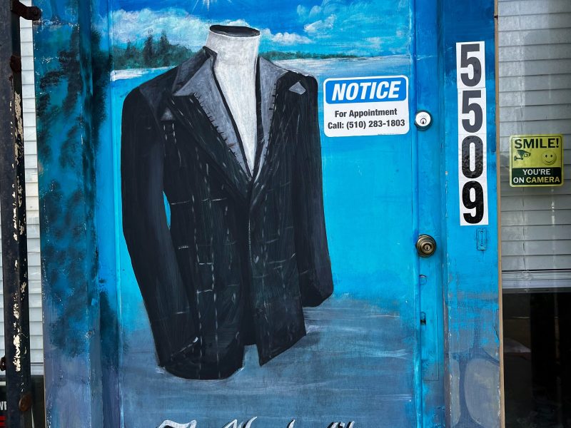 A blue door painted with a headless suit and the words "The Way he fits"; appointment notice, address number 5509, and surveillance signs are visible.