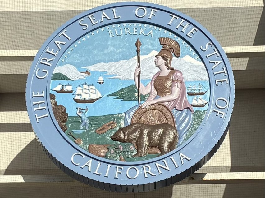 The Great Seal of the State of California featuring a grizzly bear, a female figure with a spear, ships, mountains, and the word "Eureka" on a blue circular background.