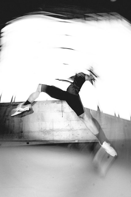 A person in athletic clothing is captured mid-leap in a blurred, dynamic motion against a bright background.