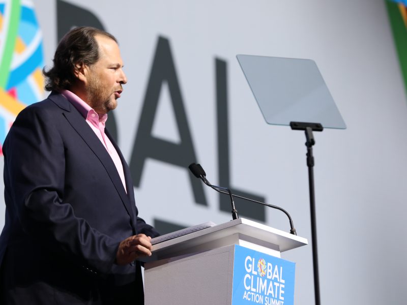 A man in a suit speaks at a podium labeled "Global Climate Action Summit" with a microphone and teleprompter in front of him.