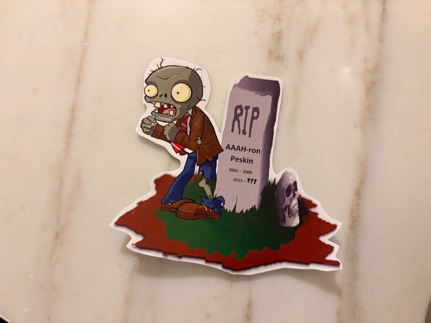 A cartoon zombie stands next to a gravestone labeled "RIP AAAH-ron Peskin 2001–2009, 2015–??" on a marble surface.