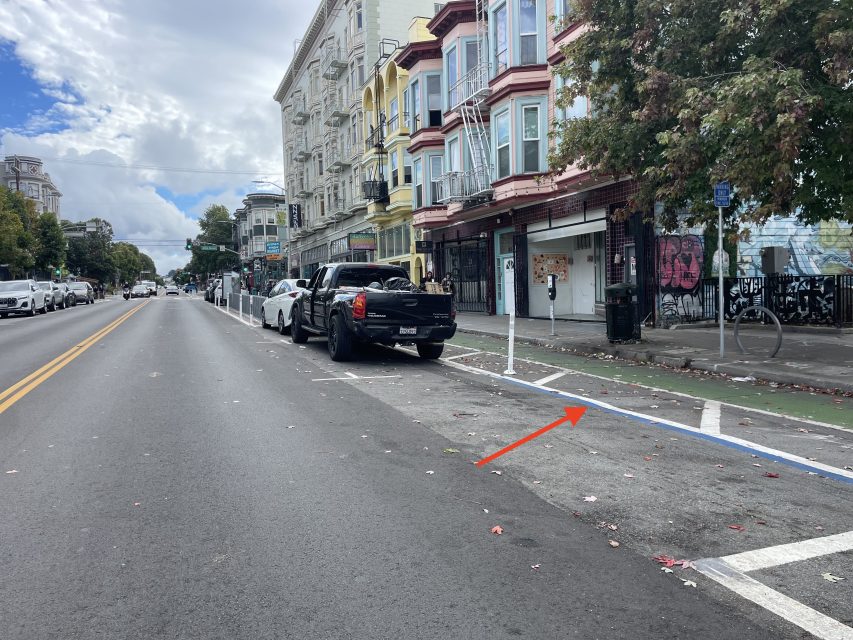 A black pickup truck is parked partially in a bike lane on a city street, with a red arrow pointing at the truck and nearby bike lane markings.