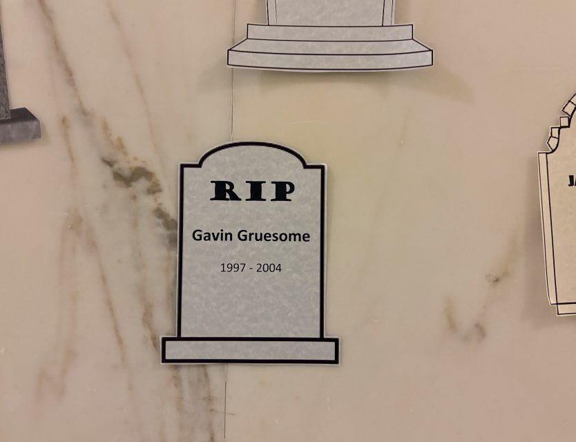 A paper tombstone with the text "RIP Gavin Gruesome 1997 - 2004" is displayed on a marble wall.