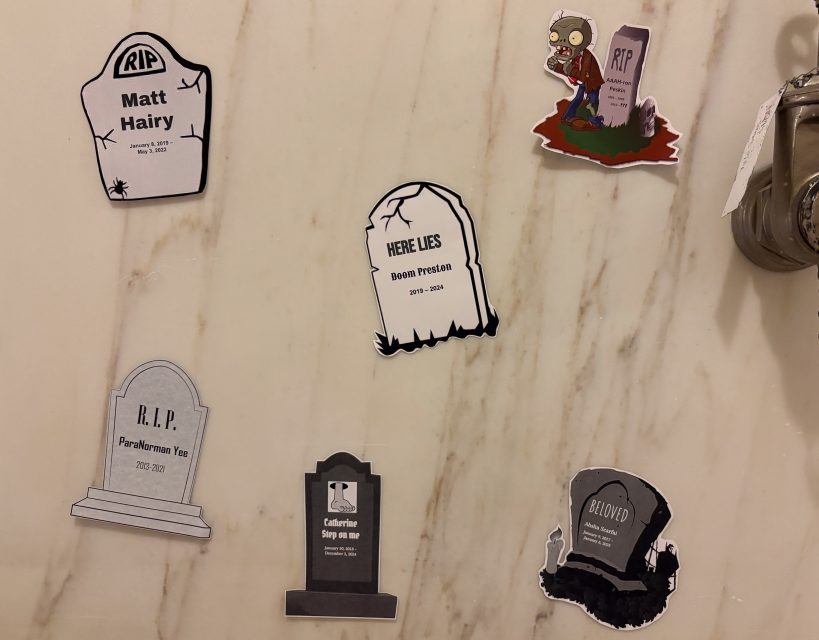 Six tombstone-shaped Halloween stickers with humorous epitaphs are displayed on a marble surface, along with a cartoon zombie sticker.
