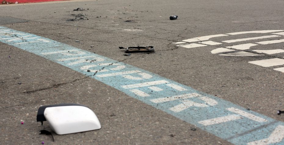 Broken car parts scattered on an asphalt parking lot near a blue line that reads "PROPERTY.