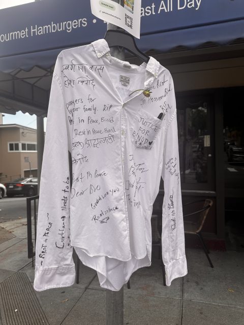 A white shirt hangs on a street sign in Bernal, covered in handwritten messages and signatures expressing condolences and calling for justice for Bendji.