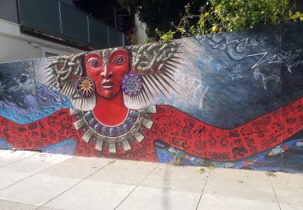 Mural of a red-skinned figure with ornate jewelry, large earrings, and patterned arms, set against a decorated background with abstract and nature motifs.