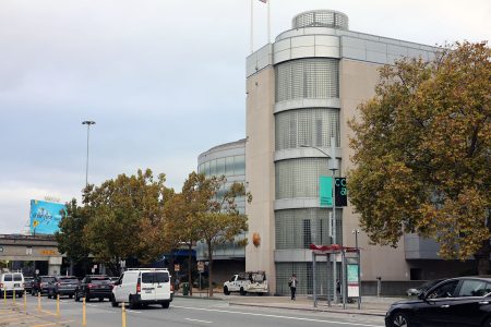 A street scene shows light traffic, a sidewalk, trees with autumn leaves, and a modern building with glass block windows and rounded corners.