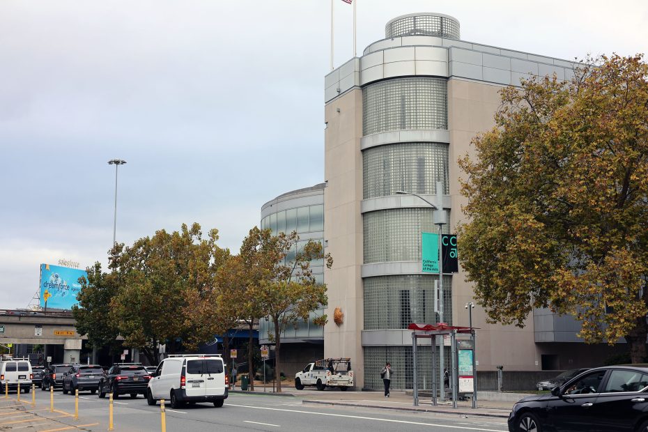 A street scene shows light traffic, a sidewalk, trees with autumn leaves, and a modern building with glass block windows and rounded corners.