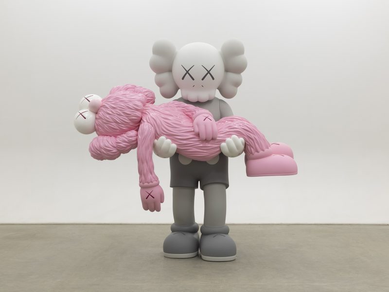 A gray cartoon-like figure with crossed-out eyes holds a pink, furry figure with similar features in its arms, standing on a plain concrete floor against a white wall.
