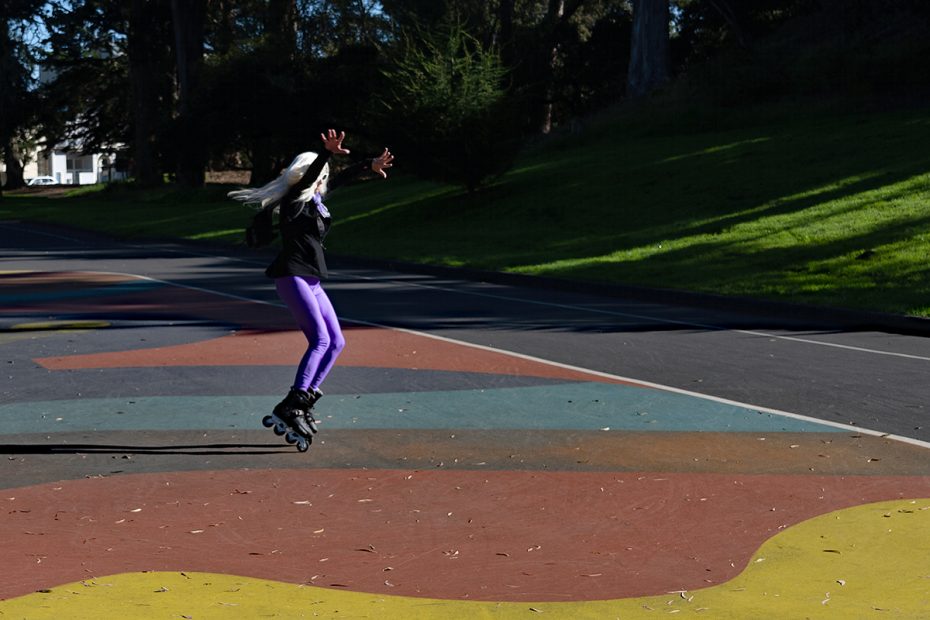 A person wearing purple pants and rollerblades is mid-air on a colorful outdoor path in a park.