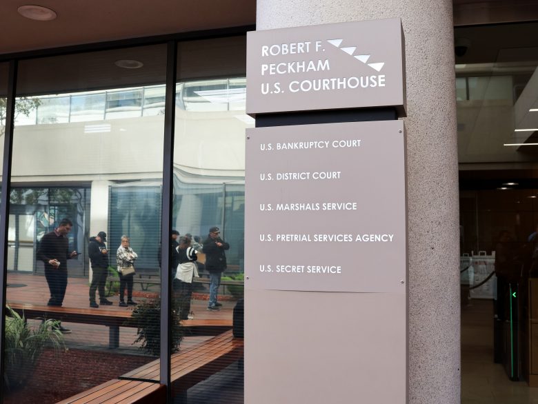 Sign outside the Robert F. Peckham U.S. Courthouse lists various federal offices; people are visible through the glass in the background.