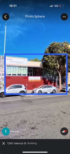 A two-story building with a red brick lower level and large windows, with two cars parked in front and a tree to the right, located at 1240 Valencia St.