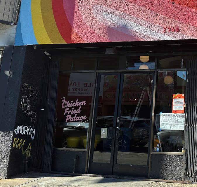 Street view of the entrance to Chicken Fried Palace, with colorful mural above, glass doors, and signs posted on the building.