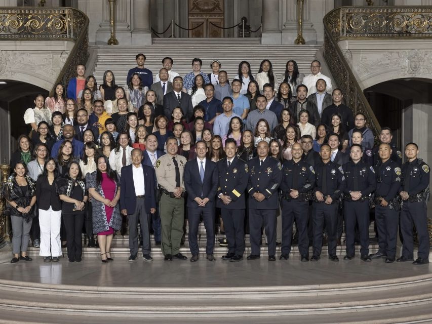 A large group of people, including uniformed officers and civilians, pose for a formal photo on the steps inside an ornate building.