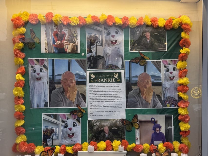 A memorial display for Frankie features photos of an elderly man, a person in a bunny costume, colorful flowers, candles, and butterfly decorations on a green background.