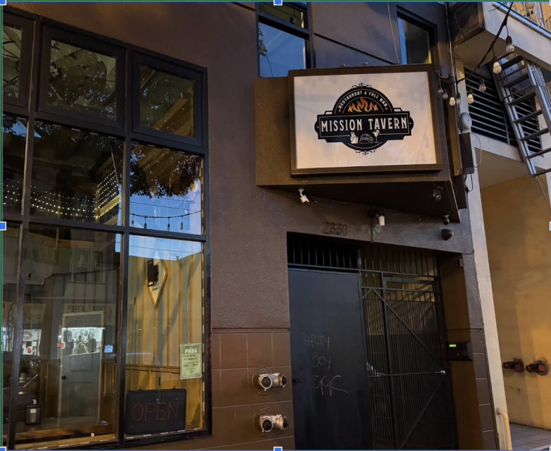 The exterior of Mission Tavern at night, showing a lit sign above a gated entrance and a window with an illuminated "OPEN" sign.