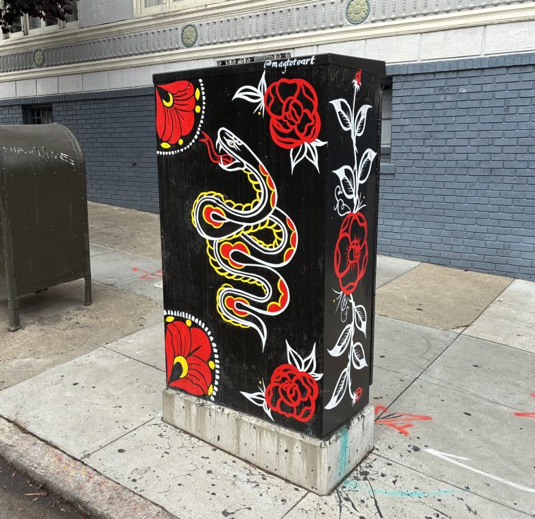 A black utility box features painted red flowers, white leaves, and a yellow snake with red markings, located on a city sidewalk beside a mailbox.