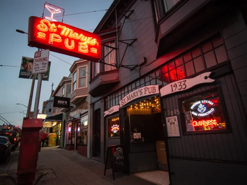 Exterior of St. Mary’s Pub at dusk with neon signs lit, including a red “St. Mary’s Pub” sign above the entrance and a Guinness sign in the window.