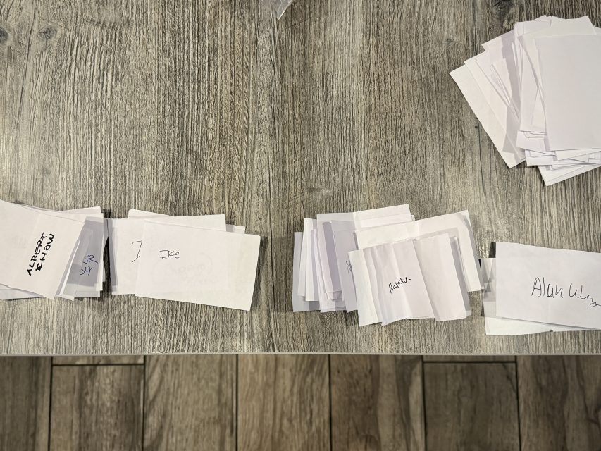 Several stacks of white paper slips with handwritten notes are arranged on a wooden table, with more slips on the right than the left.