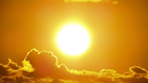 Bright sun shining in a clear sky above dark clouds, creating a vivid yellow and orange glow.
