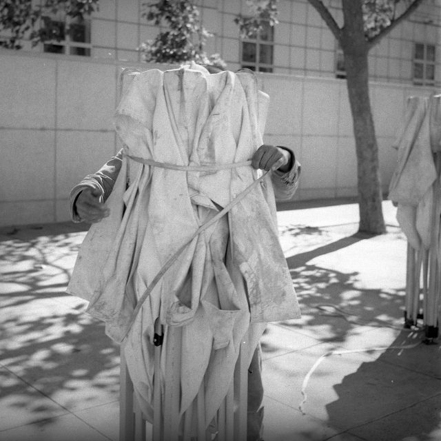 A person stands outdoors holding parts of a collapsed canopy tent, mostly hidden behind the folded fabric and metal frame.
