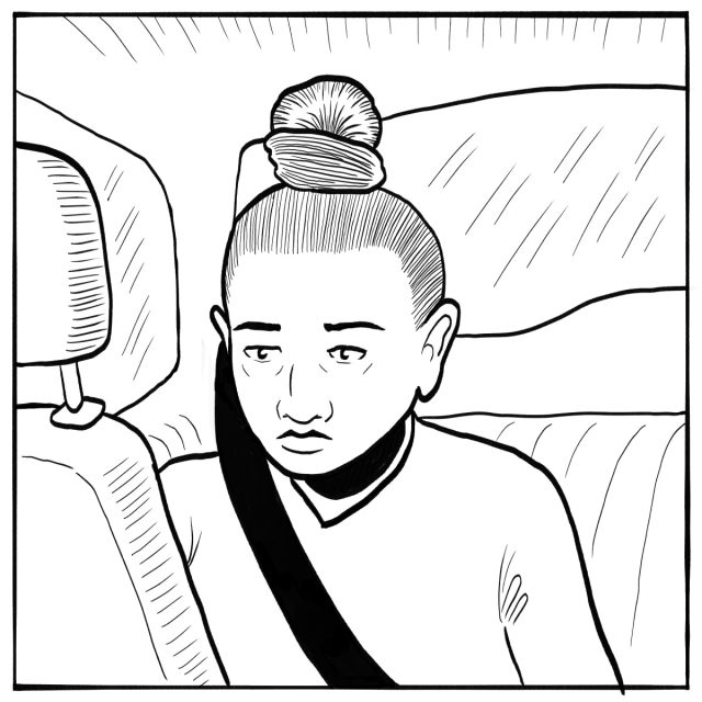 A person with a top bun hairstyle sits in a car's back seat, wearing a seatbelt and looking forward with a neutral expression.