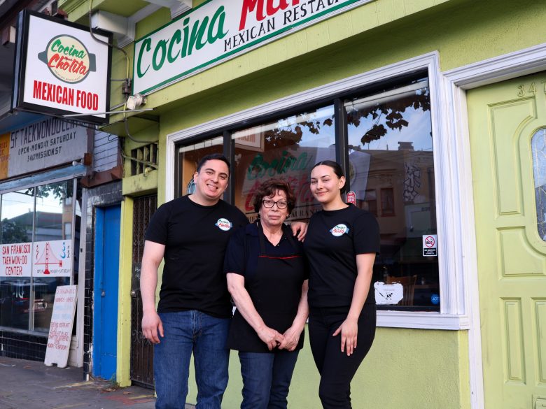 Three people stand in front of a green restaurant storefront with a sign that reads "Cocina Maribel Mexican Restaurant.