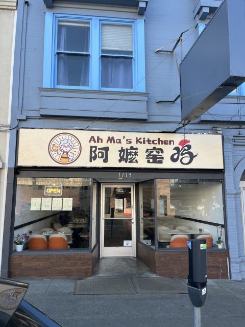 Street view of Ah Ma's Kitchen restaurant with a bilingual sign, glass front, visible tables and chairs inside, and an "OPEN" sign in the window.
