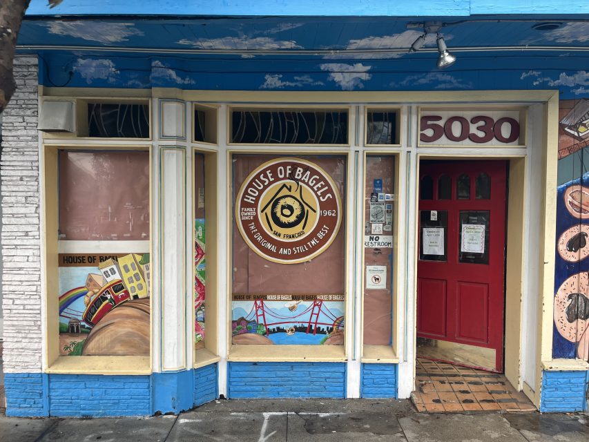 Storefront of House of Bagels with a central logo, murals on the windows, a red door to the right, and the number 5030 above the entrance.