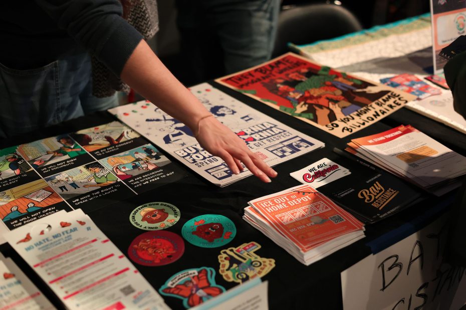A person reaches for pamphlets and colorful flyers displayed on a table at an indoor event or fair.