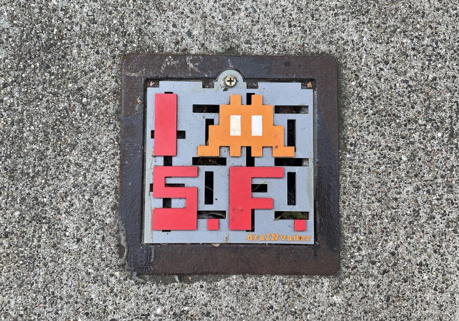 A mosaic tile on concrete reads "I [space invader] S.F." with red and orange tiles, referencing San Francisco and the Space Invaders video game character.