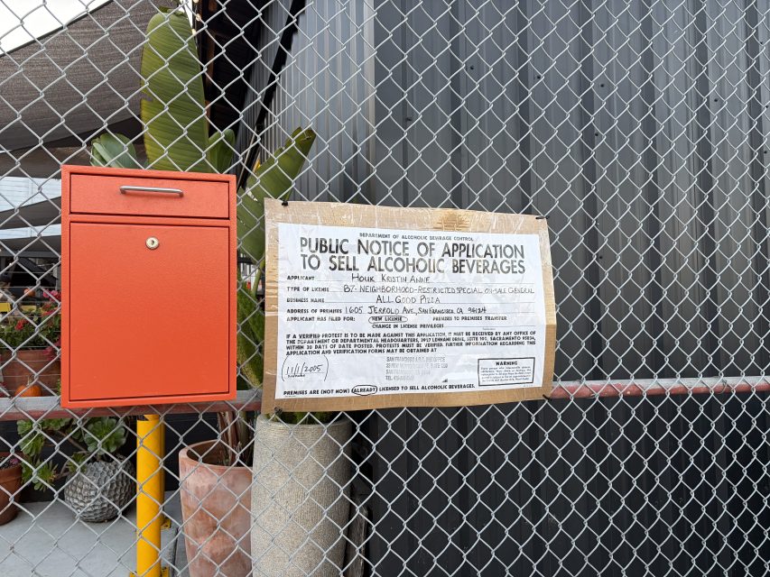 A public notice for an alcoholic beverage sale application is posted on a chain-link fence next to a red mailbox.
