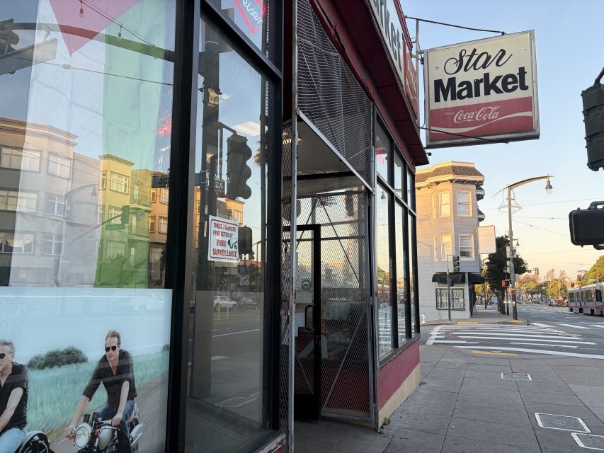 Street view of Star Market store entrance with a large sign above, glass windows reflecting buildings, and a poster of people on motorcycles in the window.
