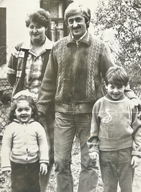 A black and white photo of two adults and two children posing together outdoors, with trees and a building visible in the background.
