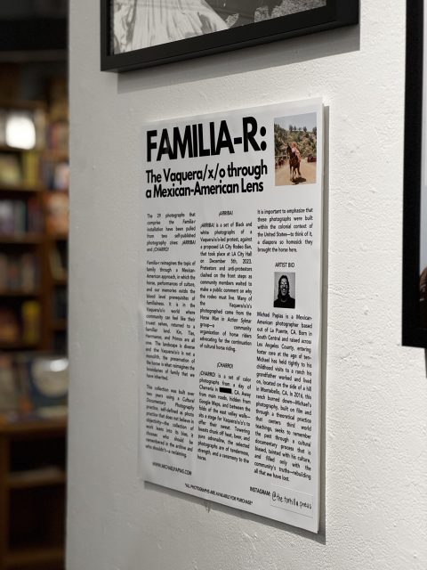 A wall-mounted poster titled "FAMILIA-R: The Vaquera/x/o through a Mexican-American Lens" with text and a small photo of people on horseback in a rural setting.