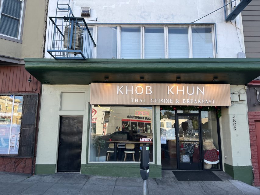 Street view of Khob Khun, a restaurant offering Thai cuisine and breakfast, with a green awning, large windows, and a parking meter in front.