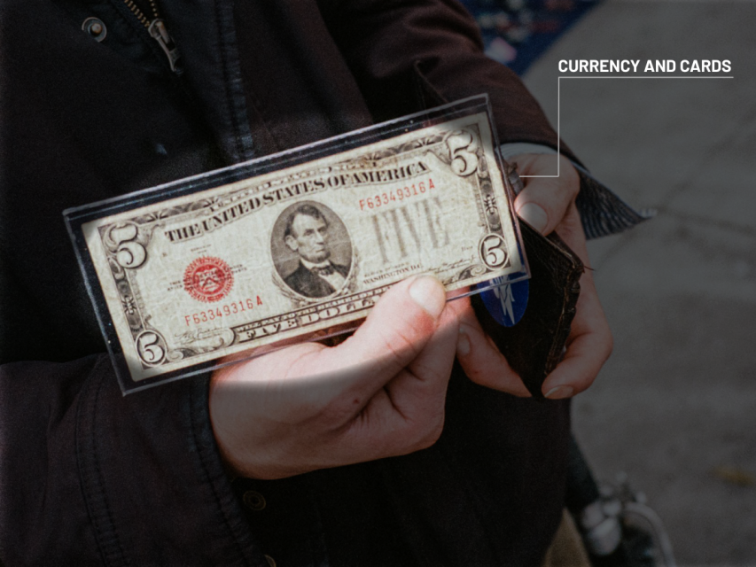 A person holds a vintage five-dollar bill in a protective sleeve, with a wallet partially visible in their other hand. A label reads "Currency and Cards.