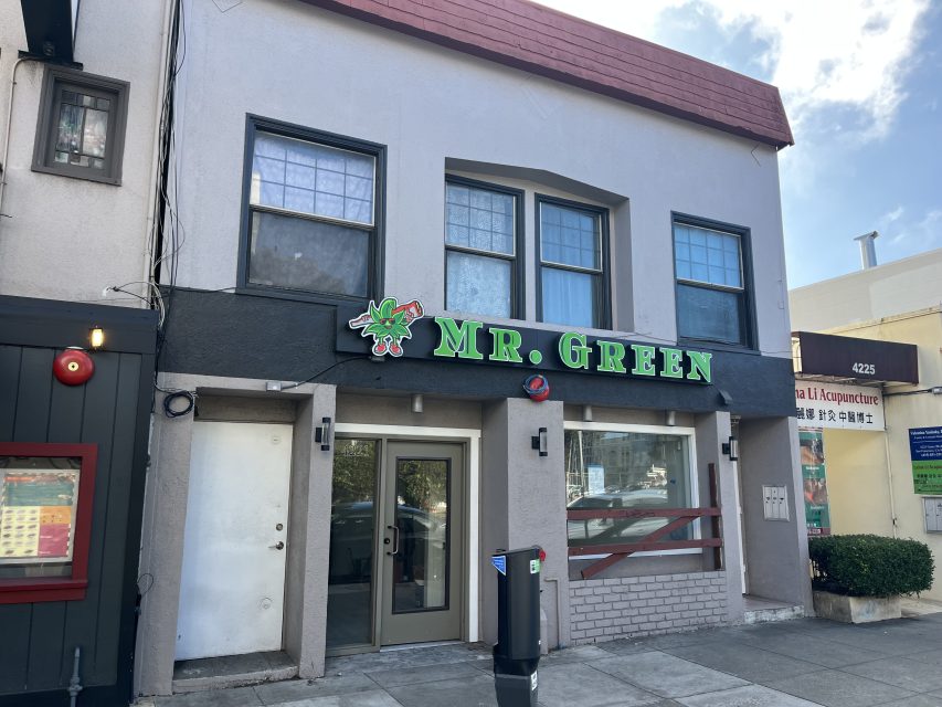 A two-story building with a sign reading "Mr. Green" above the entrance, featuring large windows and a closed door on a city street.
