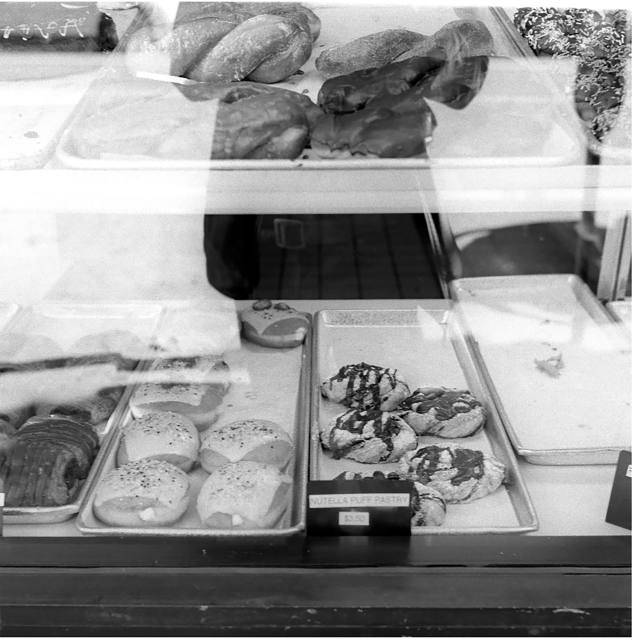 A bakery display case with trays of assorted pastries and breads, including Nutella puff pastries, viewed through the glass.