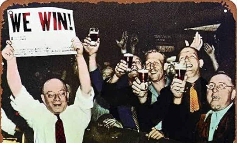 A group of men in suits cheer and raise drinks while one man holds a sign that reads “WE WIN!” in bold letters.