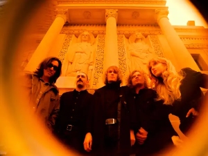 Five people stand in front of an ornate building with statues, viewed through an orange-tinted lens or filter.