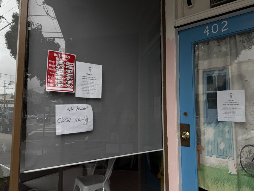 A storefront window displays a business hours sign and handwritten notice stating "No power, close early." Another notice is taped to the blue door marked with the number 402.
