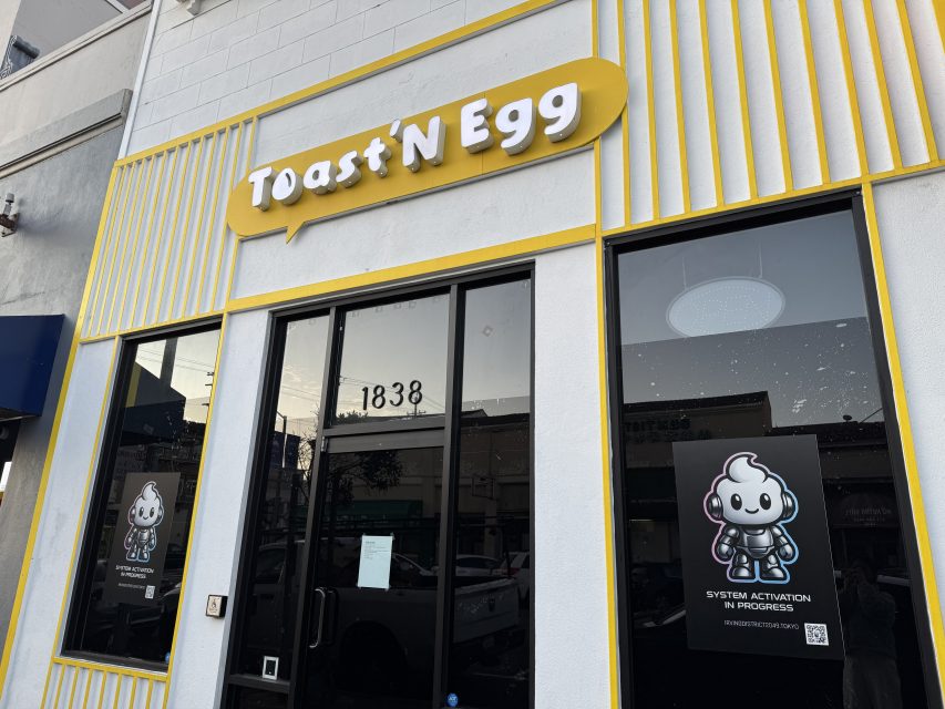 Storefront of "Toast N Egg" with street number 1838 and two posters featuring a cartoon character and the text "System Activation in Progress.