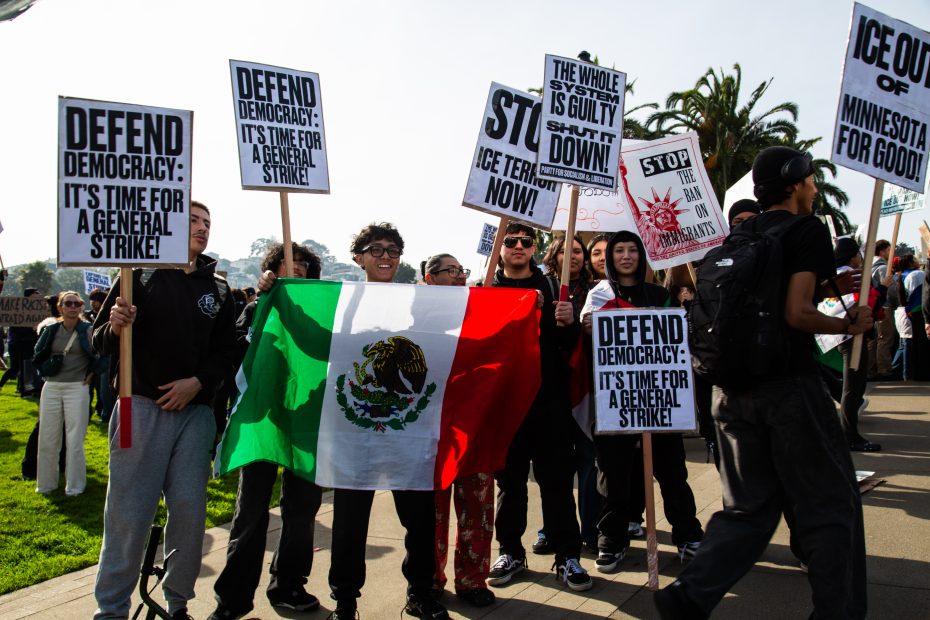Group of protesters holding signs calling for a general strike and defending democracy, with one group holding a Mexican flag; others hold signs with various protest messages.