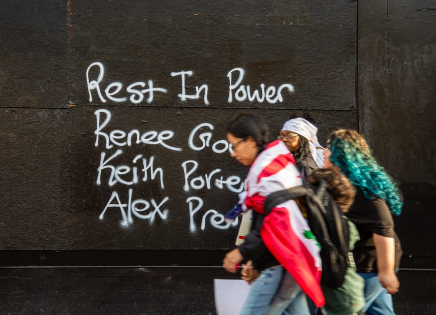 Three people walk past a black wall with white graffiti reading "Rest In Power Renee, Keith Porter, Alex" in large letters.