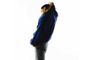 Person viewed from the side pulling a blue sweater over their head against a plain white background.